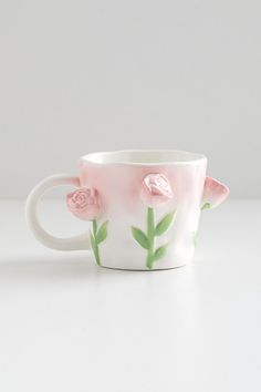 a coffee cup with pink flowers painted on the side and green leaves sticking out of it