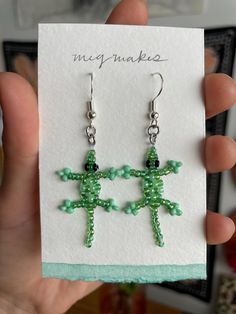 a pair of green beaded cross earrings on a white card with a hand holding it