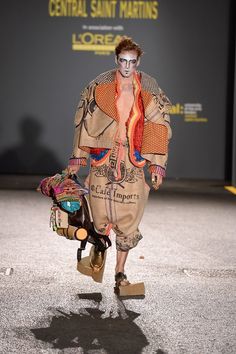 a man walking down a runway with a skateboard in his hand and painted face