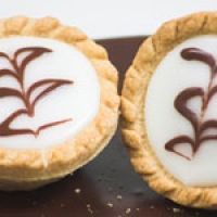 two pies with chocolate frosting on them sitting on top of a brown table