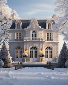 a large white house surrounded by snow covered trees and bushes with lights on the windows