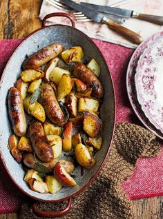 a pan filled with sausage and potatoes on top of a wooden table next to a fork