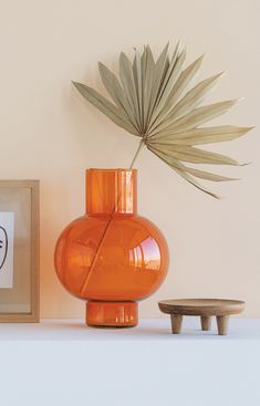 an orange vase sitting on top of a white shelf next to a small wooden table