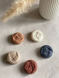 four different colored buttons sitting on top of a white surface next to a cup and feather