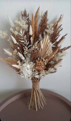 a bouquet of dried flowers sitting on top of a wooden table next to a white wall