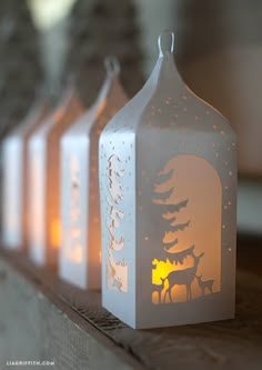 three lit candles sitting on top of a wooden table next to trees and deers