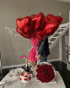 a man and woman standing in front of a table filled with red roses, cake and balloons