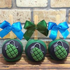 three green cake pops with blue bows and pineapples on them sitting on a wooden table