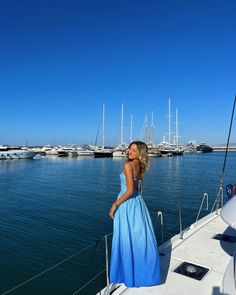 a woman in a blue dress standing on the deck of a boat looking out over the water