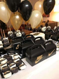 a table with black and gold balloons, white and black cakes and brown bags on it