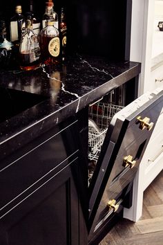 an open dishwasher sitting on top of a counter next to bottles of alcohol