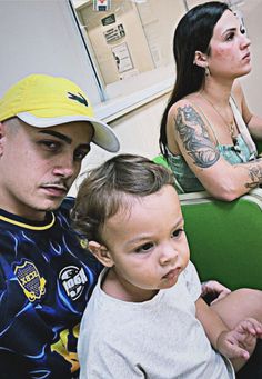 two people sitting next to each other with tattoos on their arms and chest, one holding a small child