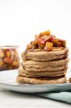 a stack of pancakes on a plate with syrup and chopped fruit in the back ground