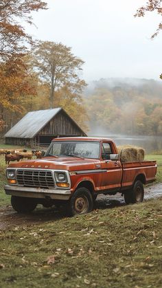 an old red pickup truck with hay in the bed is parked near a barn on a foggy day