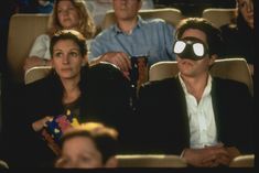 two people wearing blindfolds sitting in front of an audience at a movie theater