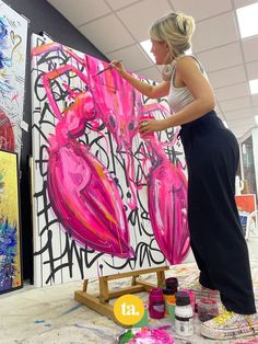 a woman is painting on the wall with pink and black art work in the background