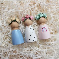 three wooden peg dolls sitting on top of some white shredded paper with flowers in their hair