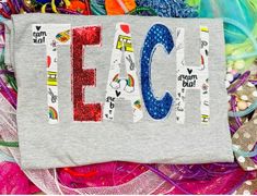 a gray t - shirt with the word teach on it surrounded by colorful fabric and beads