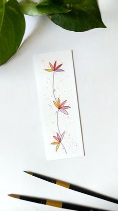 a card with watercolor flowers on it next to some paintbrushes and a plant