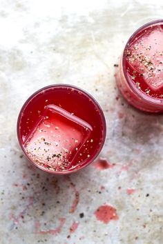 two glasses filled with liquid and sprinkles on top of a white surface