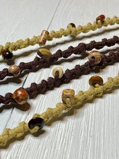 three braided bracelets with various beads on white wooden background, close up view