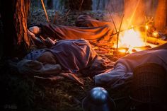 a campfire is lit up in the woods with blankets on it and two people sleeping next to it