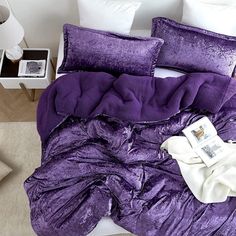 a purple comforter and pillows on a bed in a room with beige carpeting