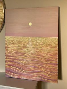 a painting on a wall with a clock in the background and a sunset over water