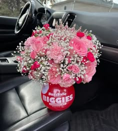 a bouquet of pink flowers in a coca - cola can on the dashboard of a car