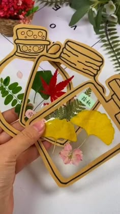 someone is holding up some paper cutouts with leaves and flowers in them on a table