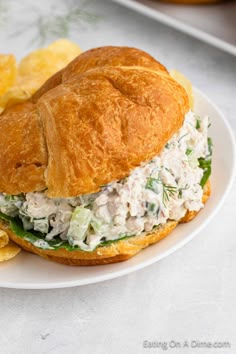 a chicken salad sandwich on a croissant bun with potato chips in the background