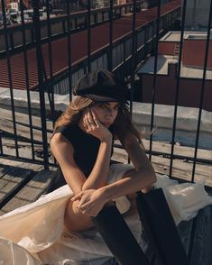 a woman sitting on top of a wooden bench next to a black fence and building