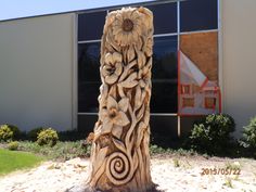 a carved wooden object in front of a building with windows and plants on the outside