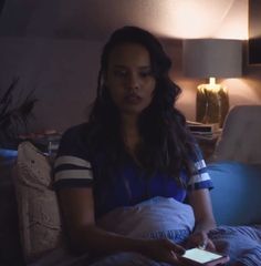 a woman sitting on a bed looking at her cell phone while holding something in her hand