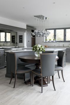 a large kitchen with an island table surrounded by gray chairs and white flowers in a vase