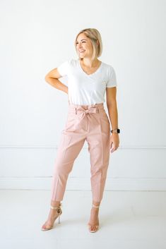 a woman standing in front of a white wall with her hands on her hips and smiling