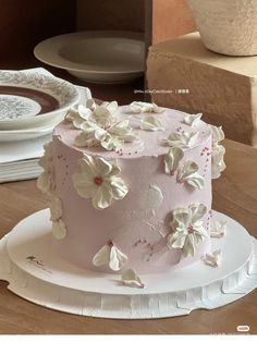 there is a pink cake with white flowers on the top and bottom, sitting on a plate