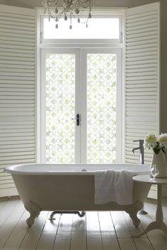 a white bath tub sitting next to a window with shutters on the outside and a chandelier above it