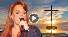 a woman with red hair singing into a microphone in front of a cross on the beach