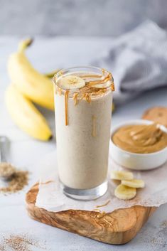 a banana and peanut butter smoothie in a glass on top of a cutting board