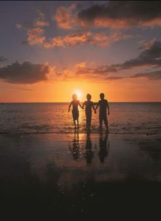 two people holding hands walking on the beach at sunset