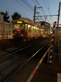 a train is coming down the tracks at night, with its lights on and buildings in the background