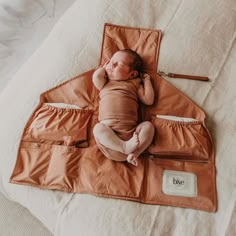 a baby laying on top of an orange sleeping bag