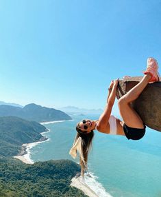 a woman climbing up the side of a cliff on top of a mountain next to water