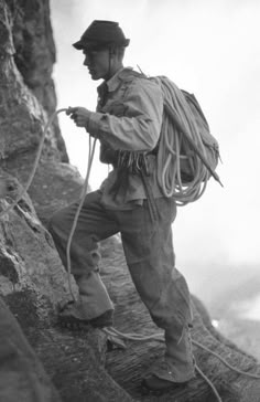 a man climbing up the side of a mountain with a backpack on his back and rope