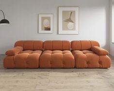 an orange couch sitting on top of a hard wood floor next to a wall with two pictures above it