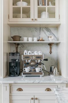 a coffee maker is sitting on the counter in front of some shelves with cups and saucers