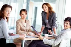 four women sitting at a table having coffee and talking to each other in an office setting