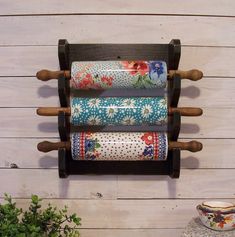 three rolls of toilet paper are hanging on a wooden rack with two cups and vases