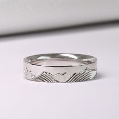 a white gold wedding band with mountains engraved on the side, set in 18k white gold